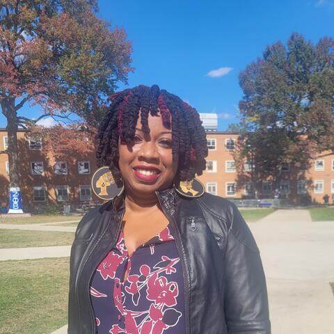 Lakeyta Bonnette smiling wearing a black leather jacket and a blouse with flowers. 